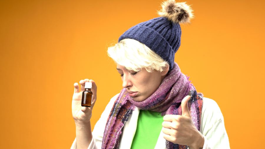 sick-unhealthy-woman-with-short-hair-warm-scarf-hat-holding-medicine-bottle-showing-thumbs-up-with-sad-expression-standing-orange-background.jpg